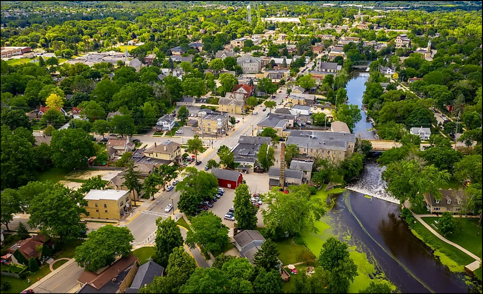 Aerial view of a Northwestern Wisconsin river town with tree-lined streets, a historic downtown, and a dam on the river